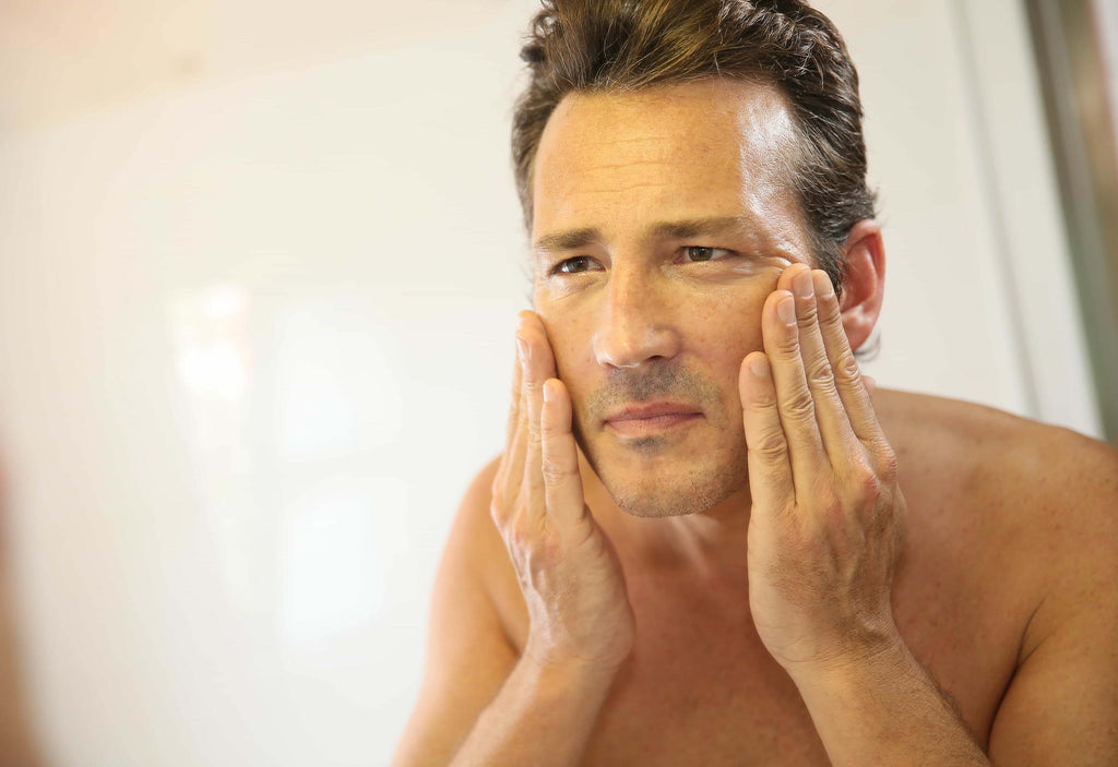 middle aged man looking at his skin in the mirror